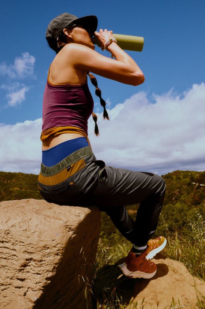 A woman hiking and drinking water from a reusable mug. Wearing eco-friendly clothes from affordable sustainable fashion brand prAna