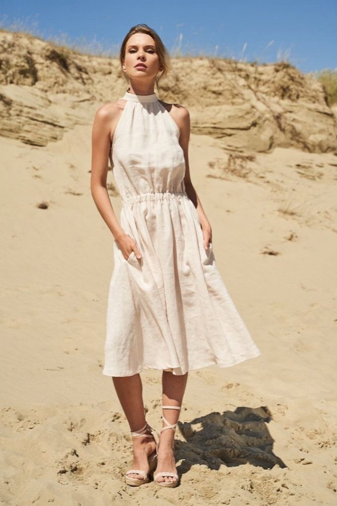 A woman on the beach wearing a white linen dress from affordable sustainable fashion brand Linen Handmade Studio