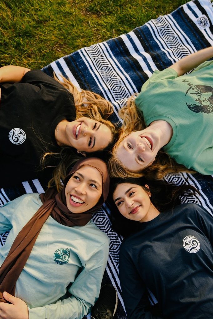 4 young girls laying on the grass wearing organic cotton t-shirts from affordable sustainable clothing brand Happy Earth