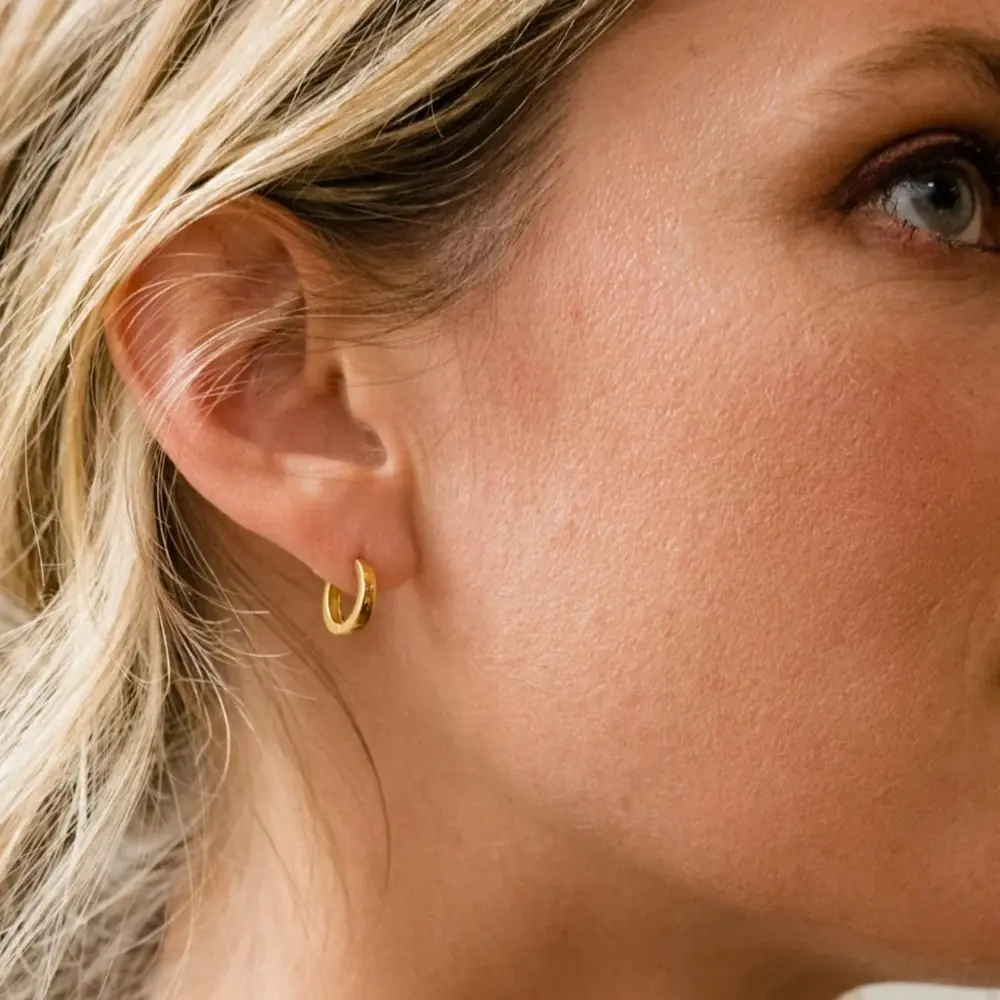 A woman wearing a pair of small gold hoop earrings from ethical brand ABLE for a sustainable capsule wardrobe everyday jewelry piece