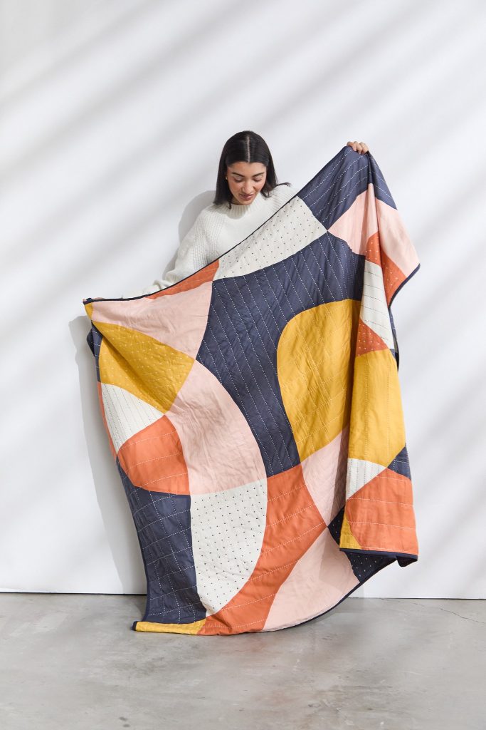 a woman holding a sustainable quilt made by a brand that empowers women, anchal