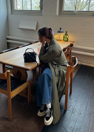 New York-based fashion influencer @poppyalmond wearing a stylish spring outfit with a trench coat and sneakers.