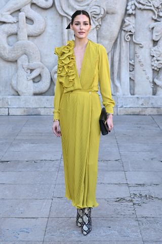 A woman wears a yellow dress and snake-print boots.