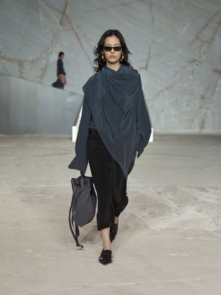 Model walking at the S/S 25 COS show in Greece wearing a gray scarf top with capri pants.