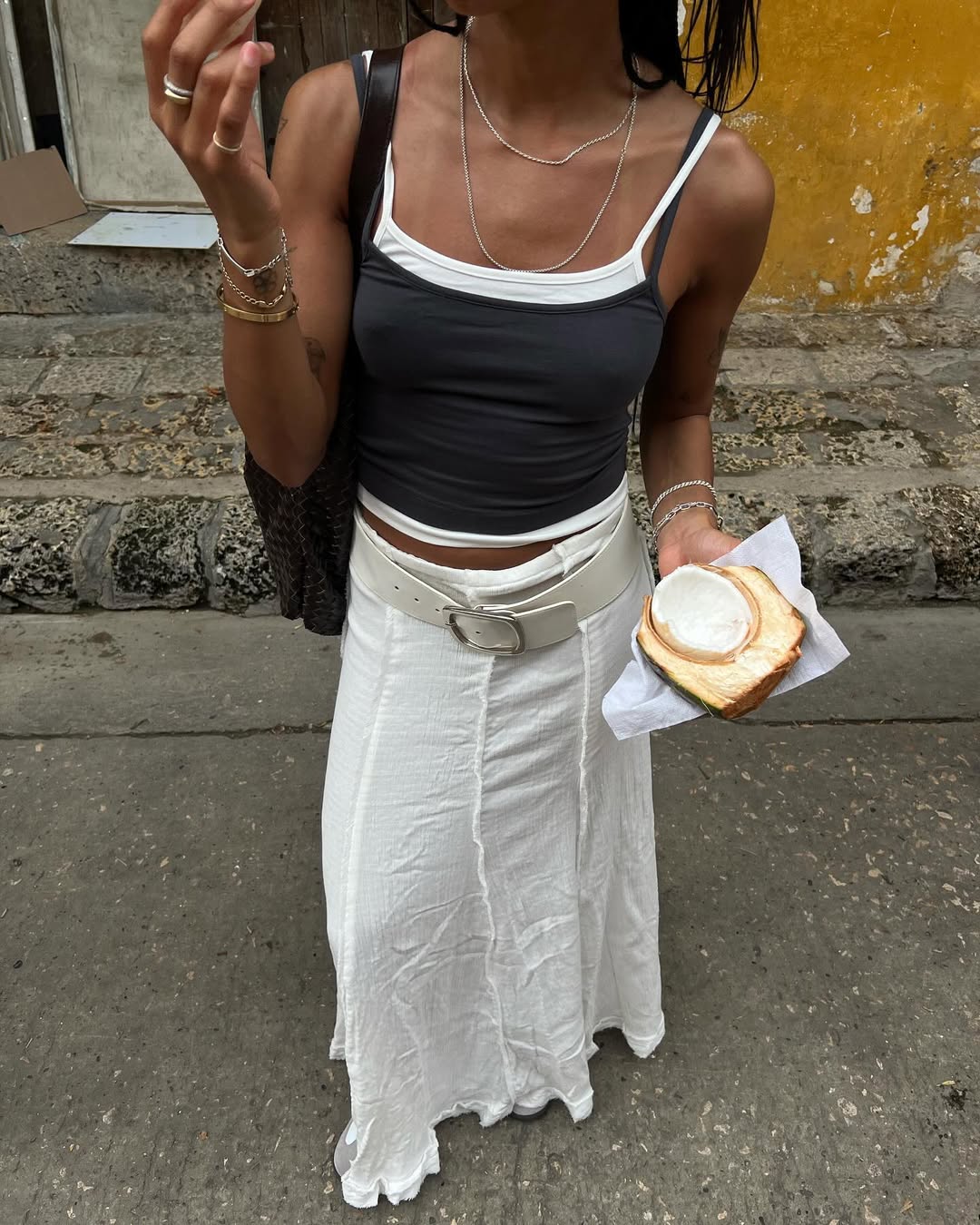 Woman wearing layered tanks and white maxi skirt with white belt in a summer 2025 outfit.