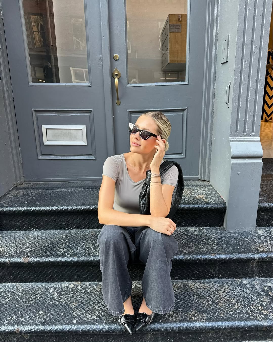 Woman wearing loose jeans with fitted gray T-shirt and black purse in a summer 2025 outfit.