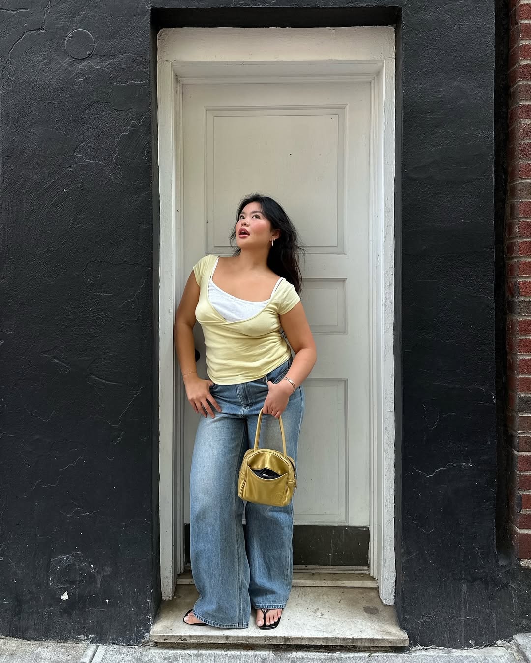 Woman wearing loose jeans with fitted yellow tank and yellow purse in a summer 2025 outfit.