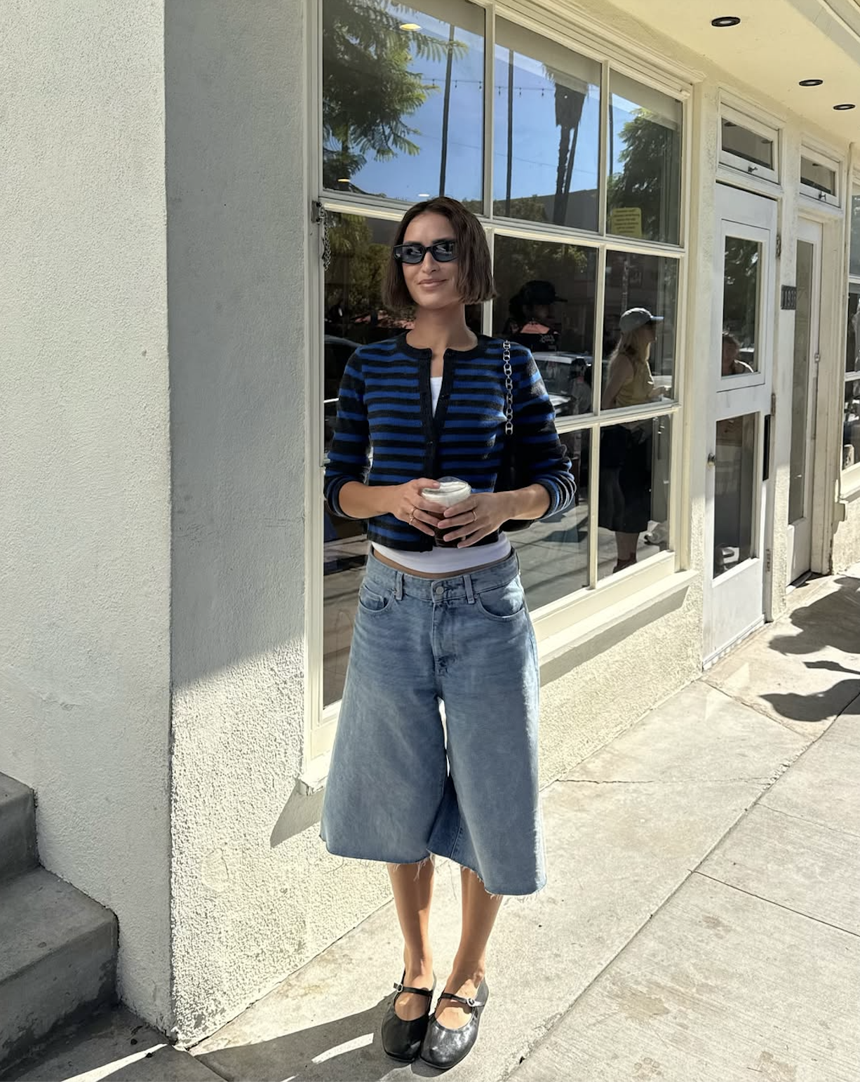 Woman wearing striped cardigan with denim long shorts and ballet flats in a summer 2025 outfit.