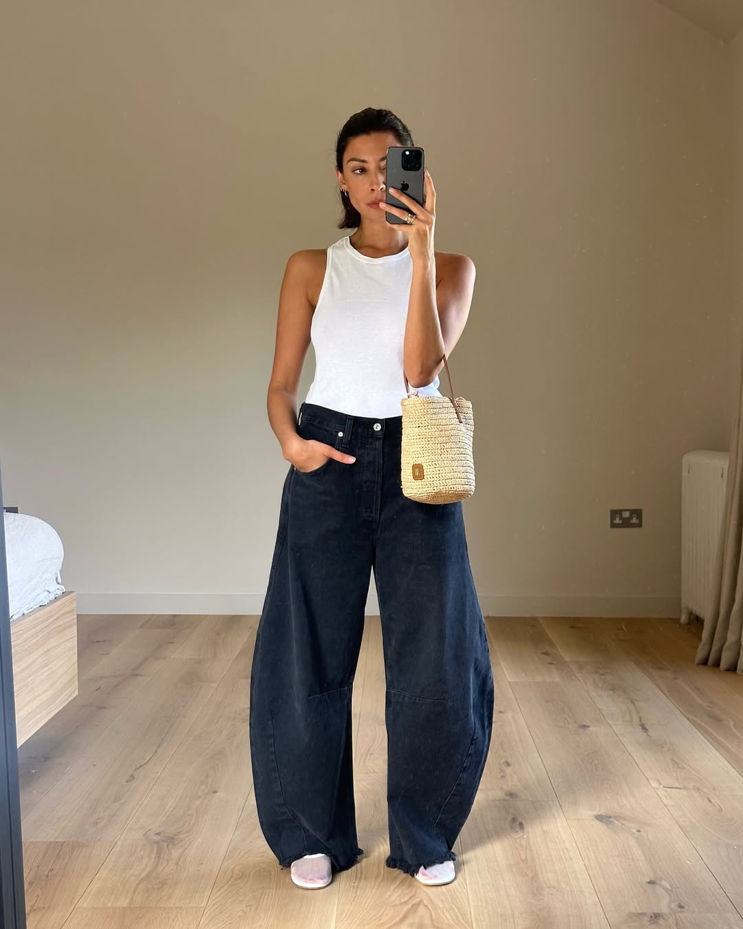 Woman wearing loose barrel jeans with fitted white tank and raffia purse in a summer 2025 outfit.