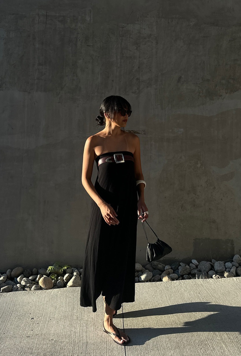 how to wear a statement belt is shown in a photo of a woman standing outside wearing a black strapless dress with black sandals and a black bag and a brown belt across the bust