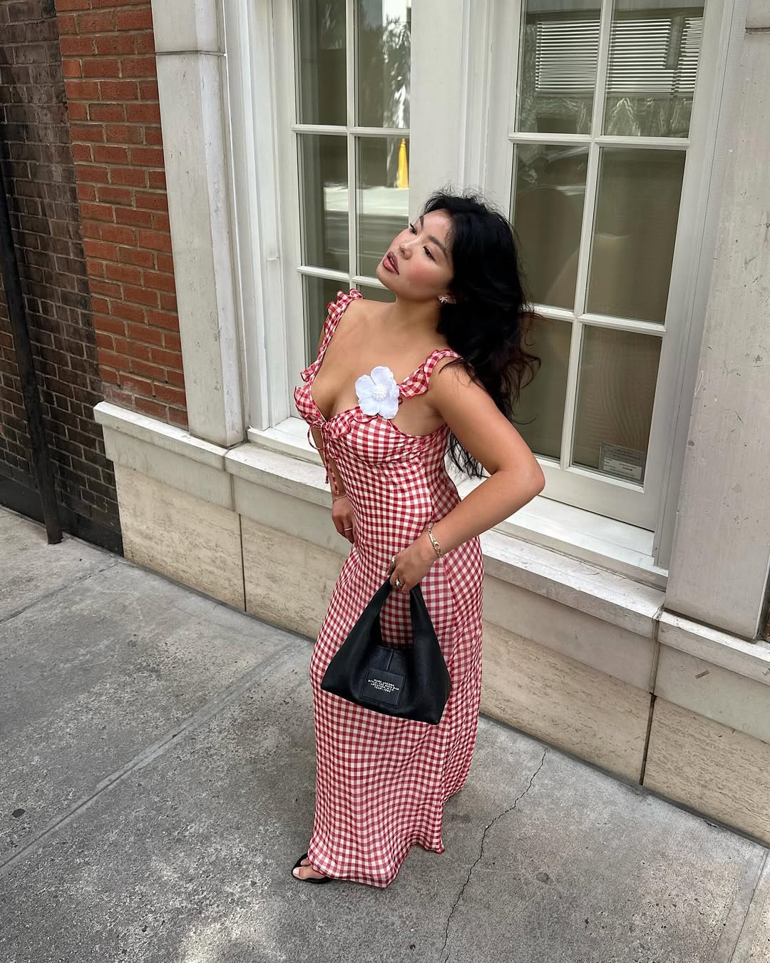 Woman wearing red and white gingham print dress with white flower in a summer 2025 outfit.