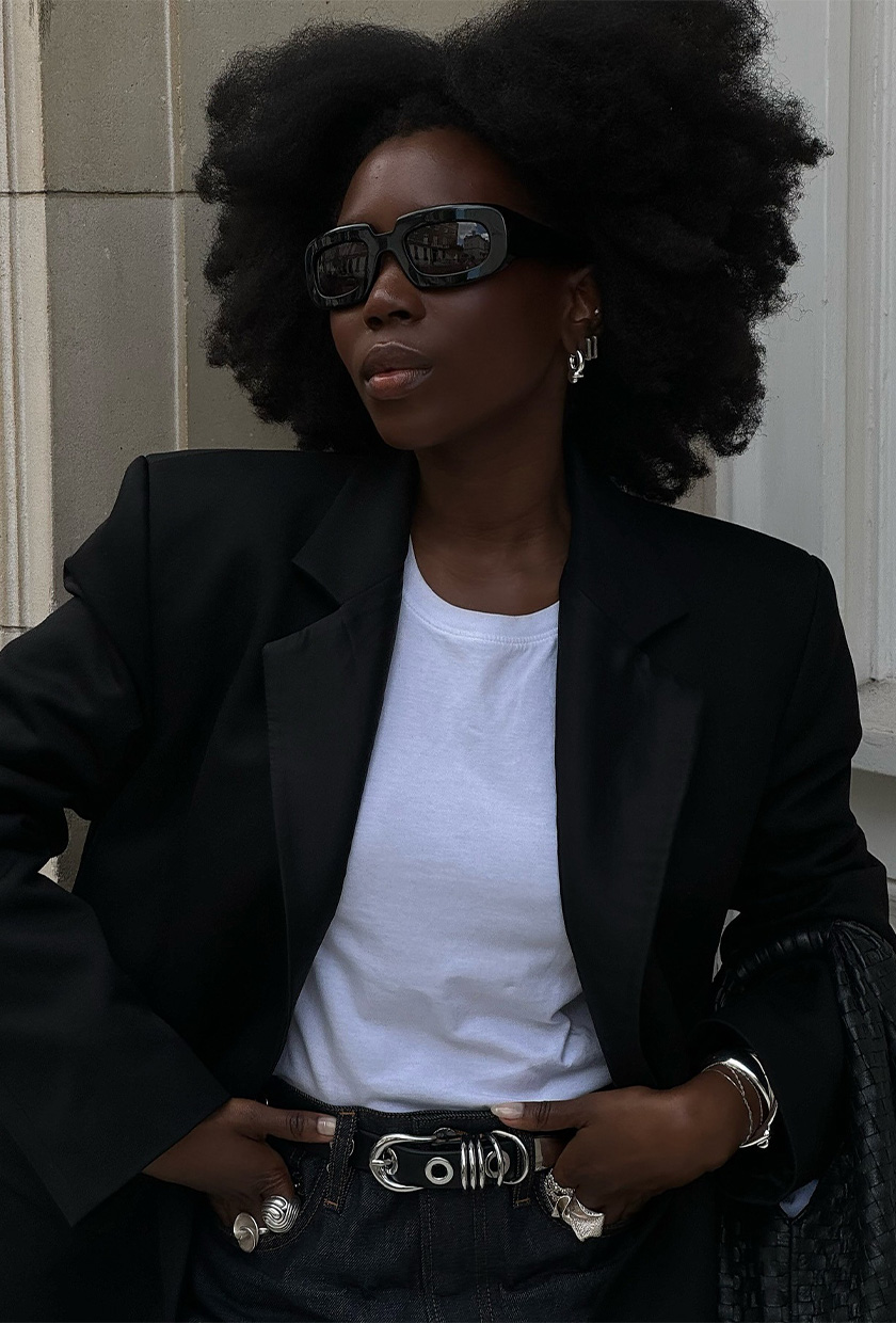 how to wear a statement belt is shown in a photo of a woman wearing a black blazer over a white t-shirt with a black studded belt and silver stacked jewelry