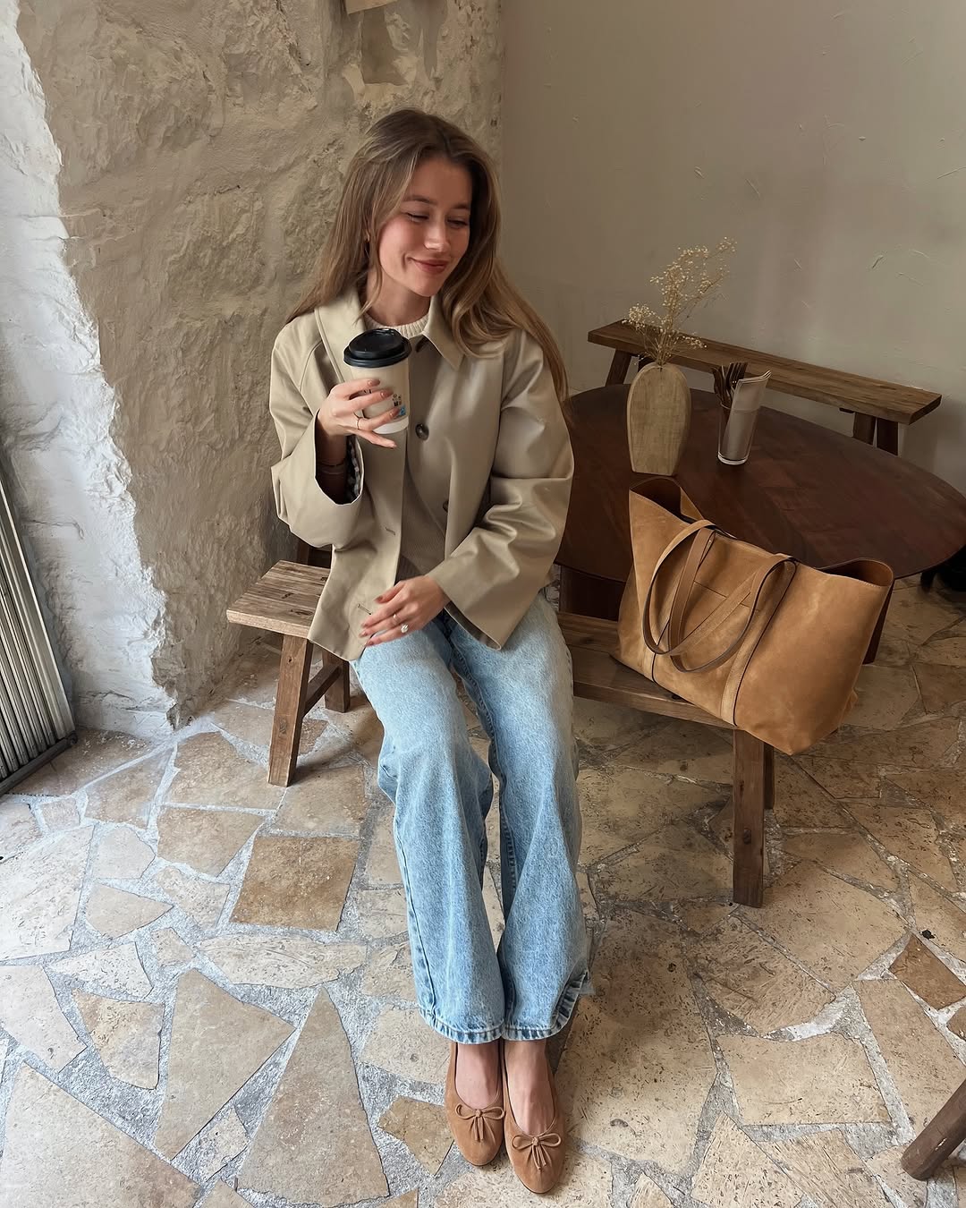 Woman wearing tan jacket and jeans with ballet flats.