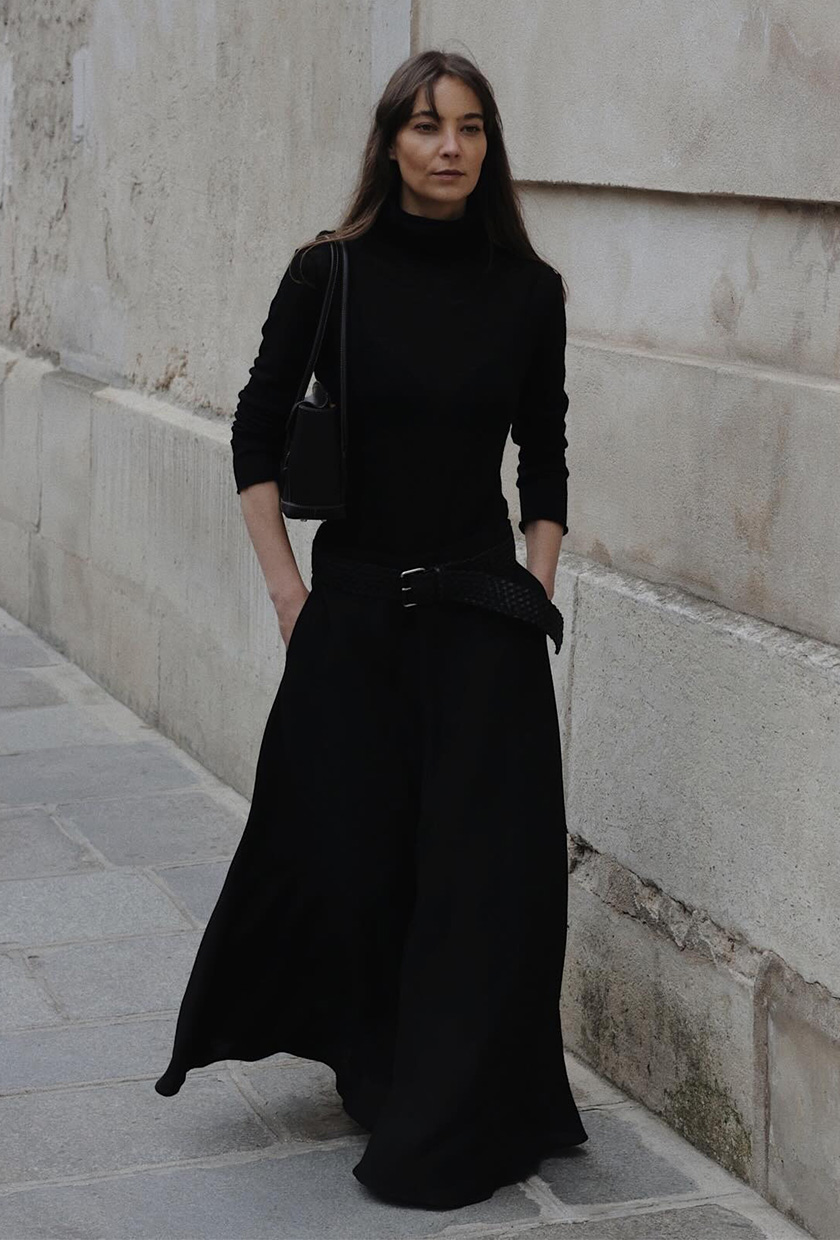 how to wear a statement belt is shown in a photo of a woman wearing a black turtleneck with a black maxi skirt and a low-slung black woven belt