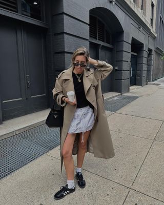 New York-based fashion influencer @hannahlewisstylist wearing a stylish spring outfit with a trench coat and sneakers.