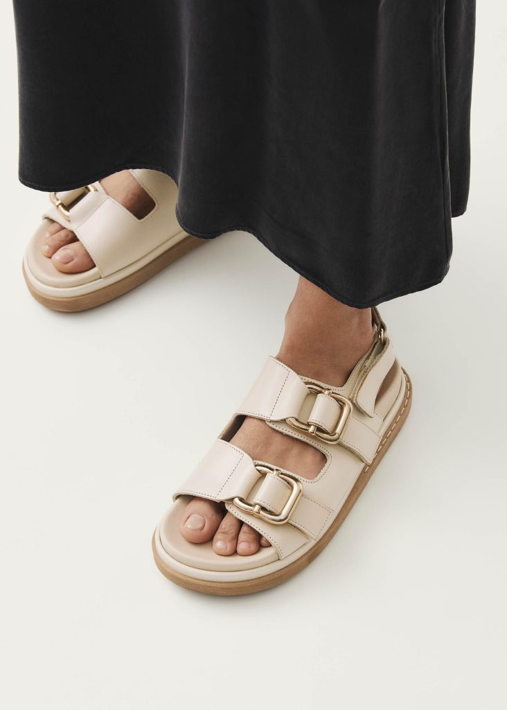 A pair of feet wearing cream sustainable sandals from ALOHAS that are a great alternative to Birkenstocks