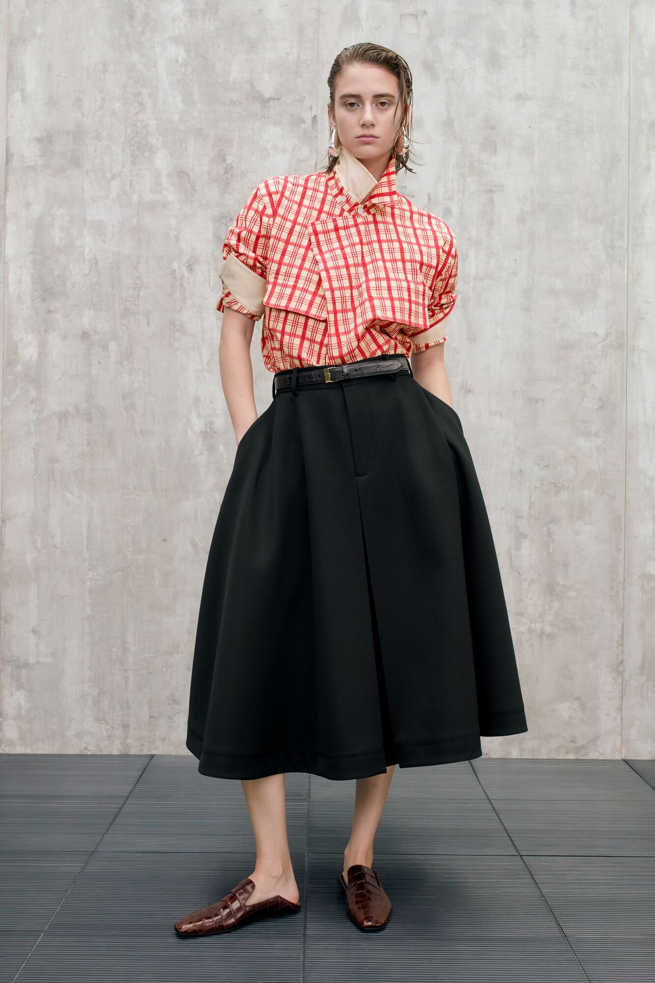 A look from Bottega Veneta's Pre-Spring 2025 collection including a red plaid shirt and black skirt. 