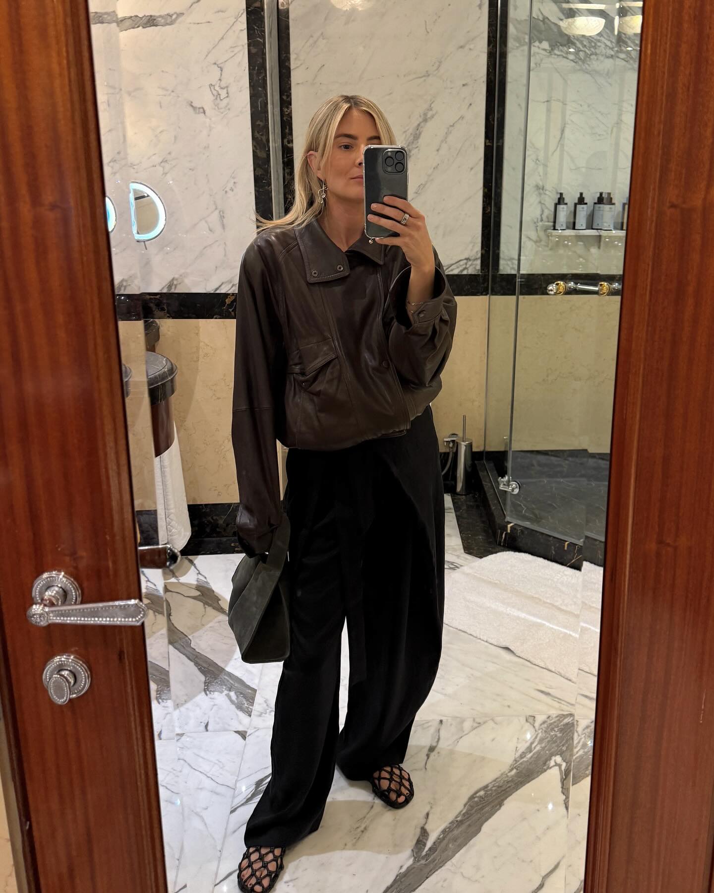 Luxy wears a leather jacket, black trousers, and caged sandals.