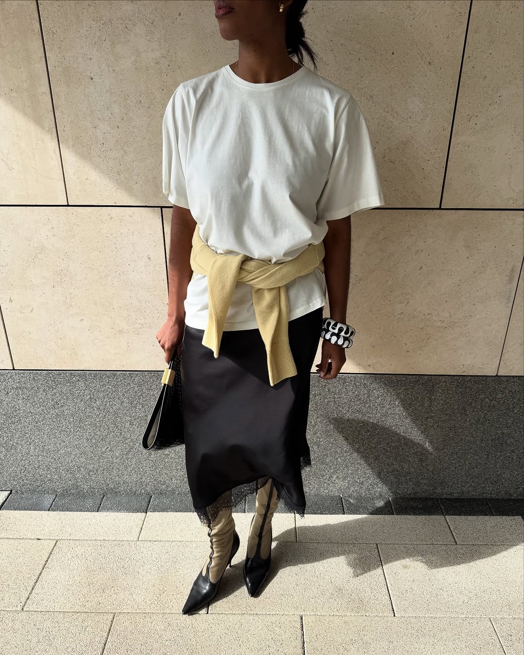 woman wearing black midi skirt, white t-shirt, and butter yellow sweater around waist