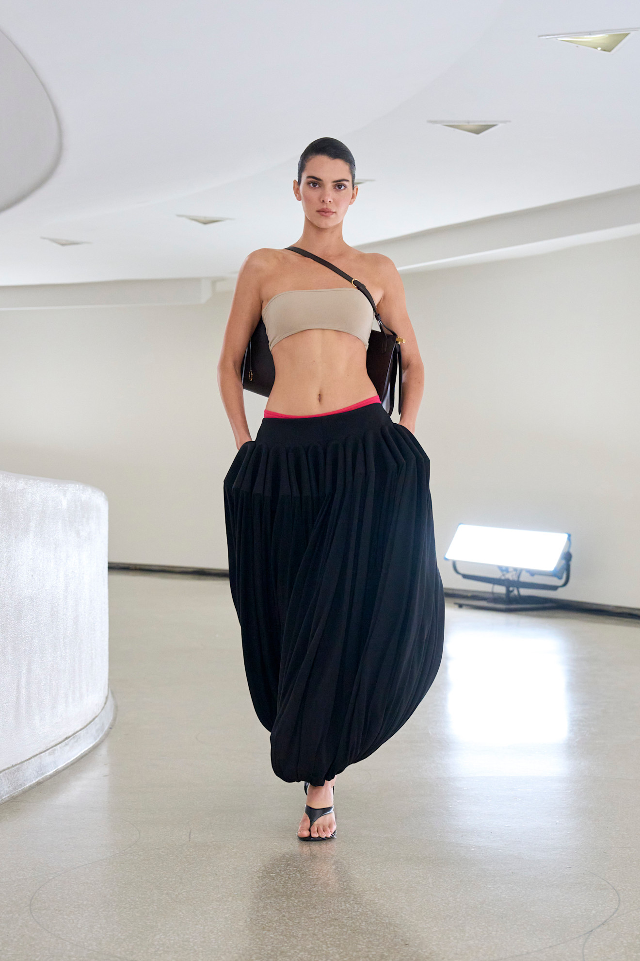 Kendall Jenner is wearing a bandeau top and black genie pants on the runway at Alaïa's spring/summer 2025 show.