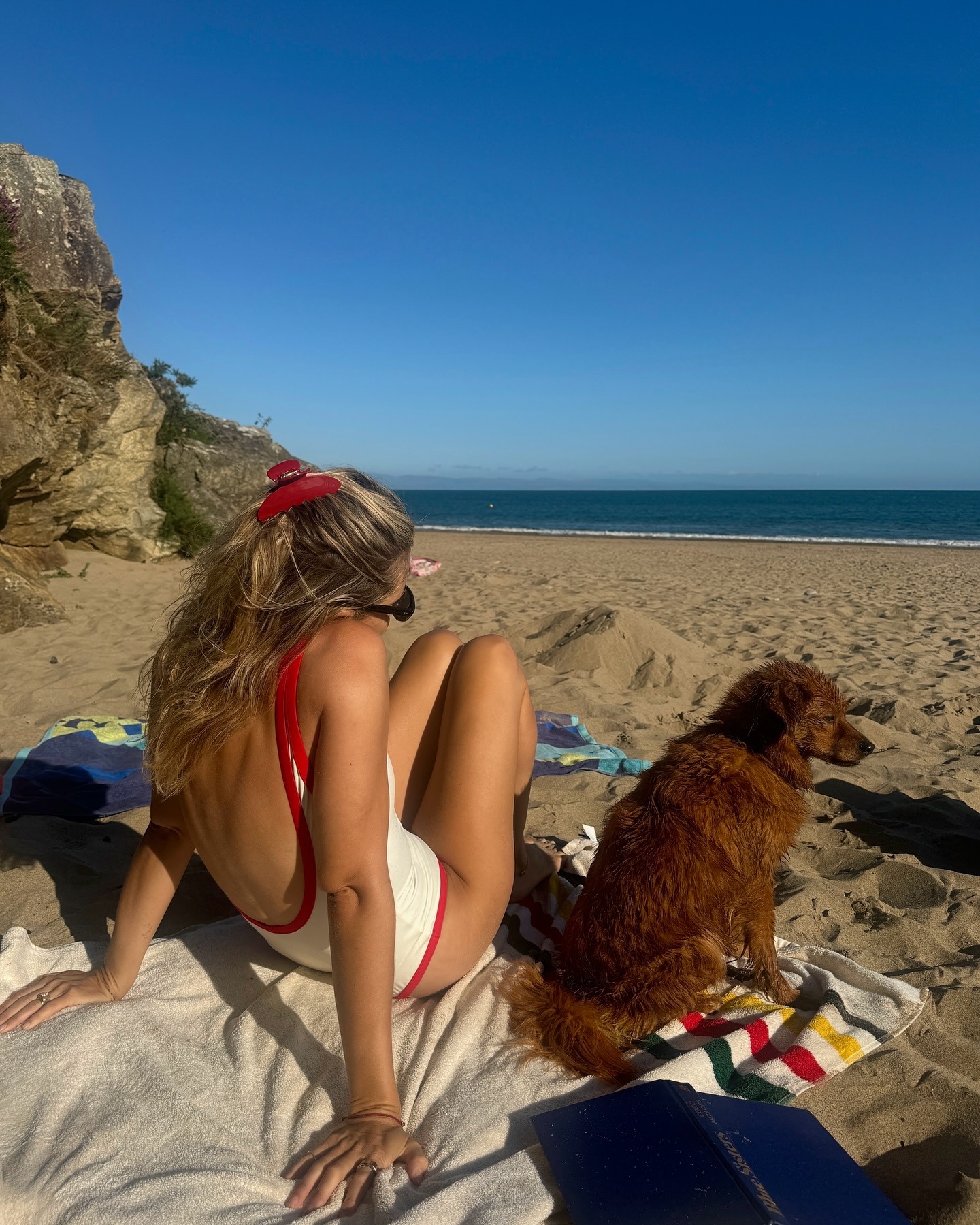 Lucy Williams wearing a red-and-cream two-tone one-piece swimsuit on the beach with her dog.