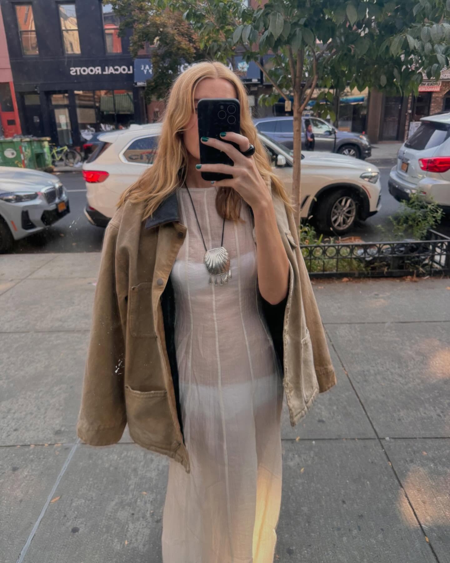 Courtney Grow wearing a barn jacket with a sheer white dress and Juju Vera shell necklace.
