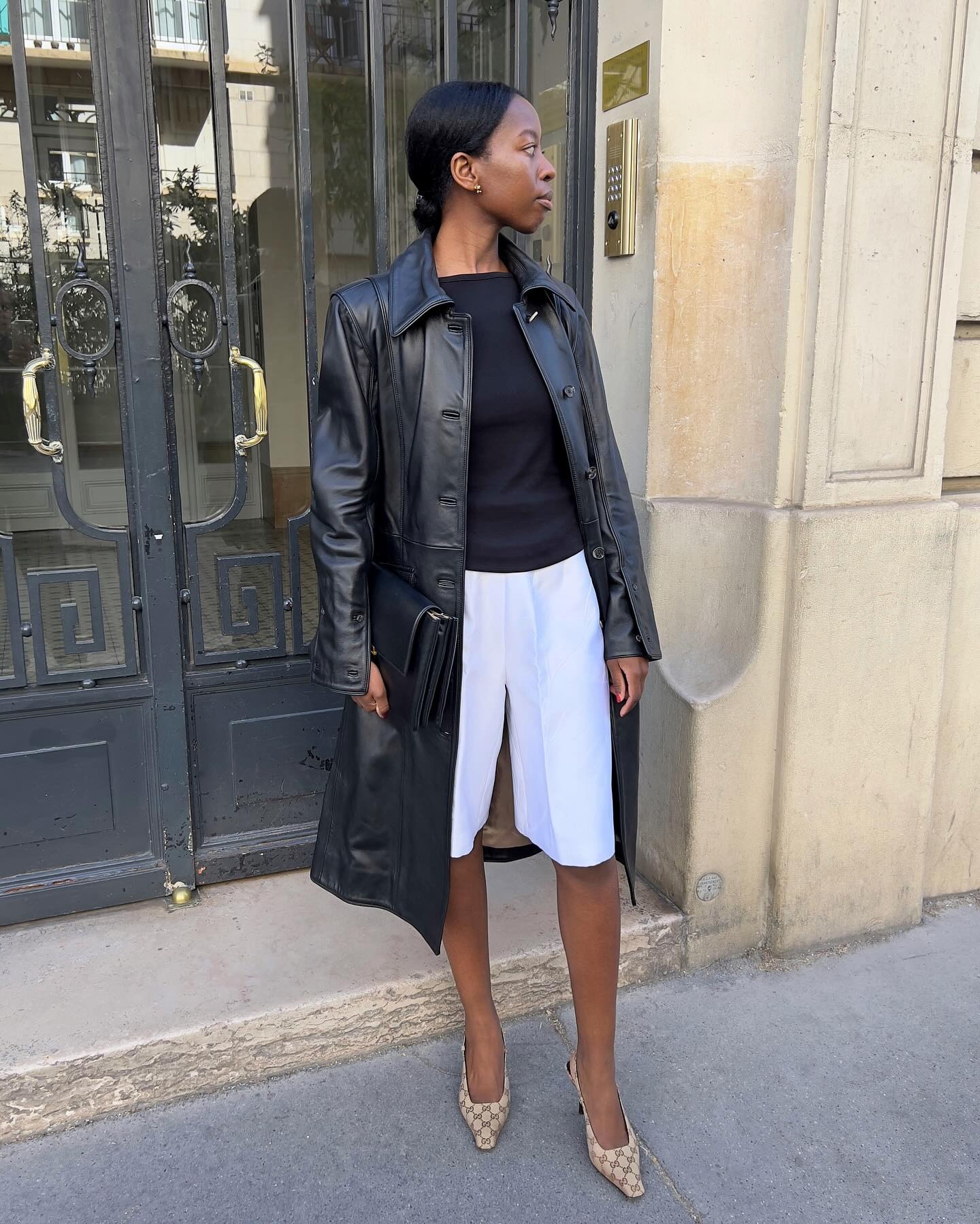 Sylvie Mus wearing a leather jacket, black top, white Bermuda shorts, and Gucci heels.