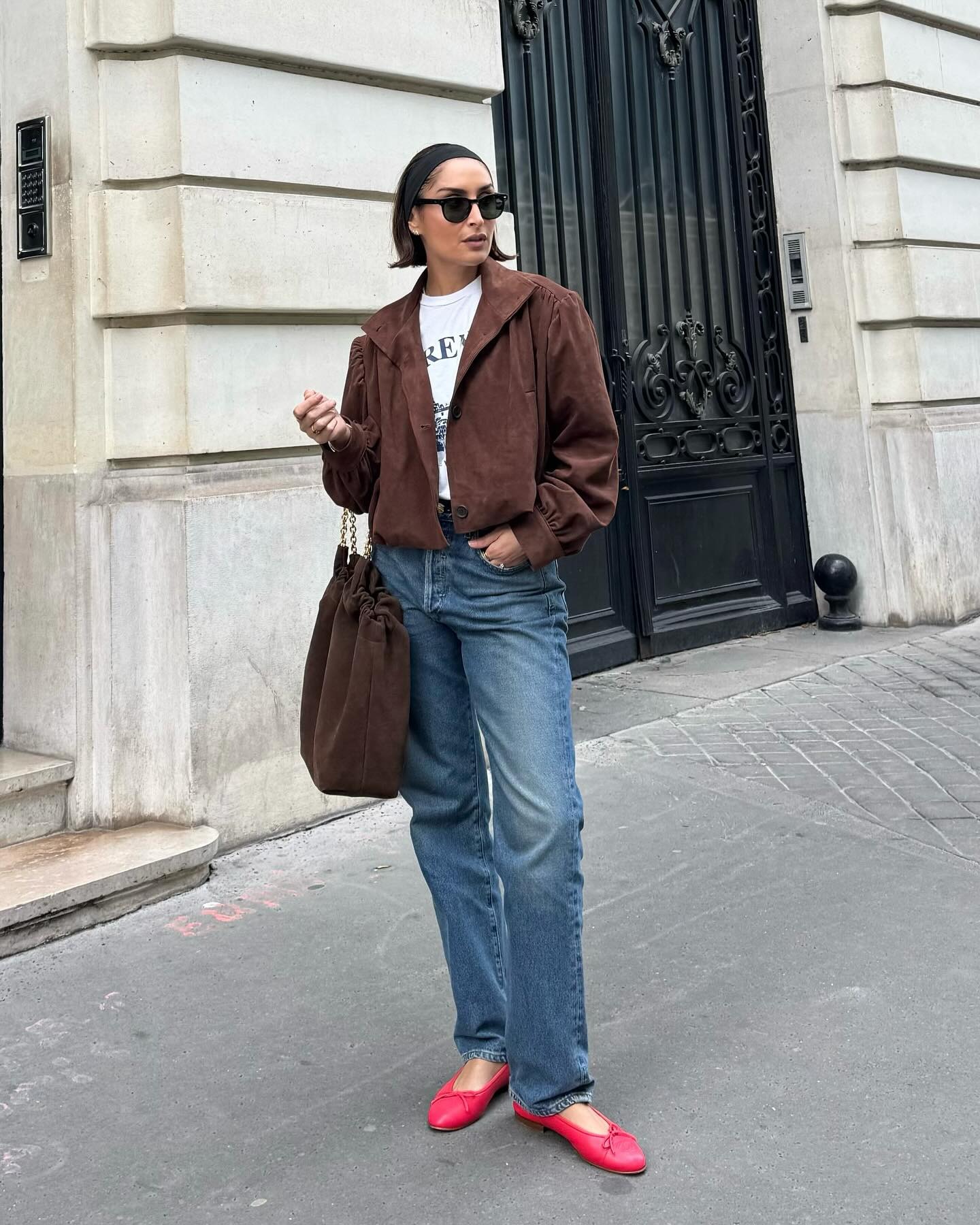 French influencer wearing a brown suede jacket, jeans, and red ballet flats