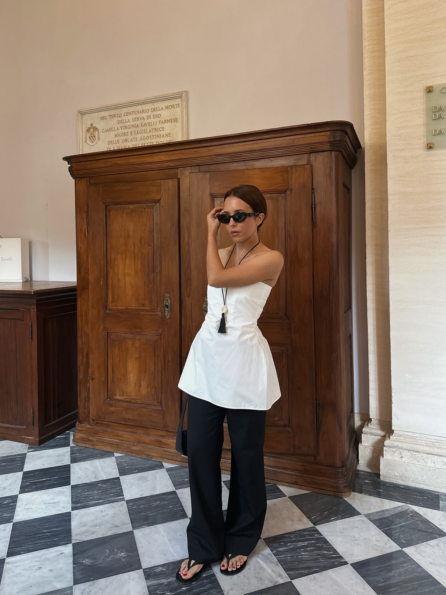 Debora Rosa wearing a white peplum top, black pants, and a tassel pendant necklace.