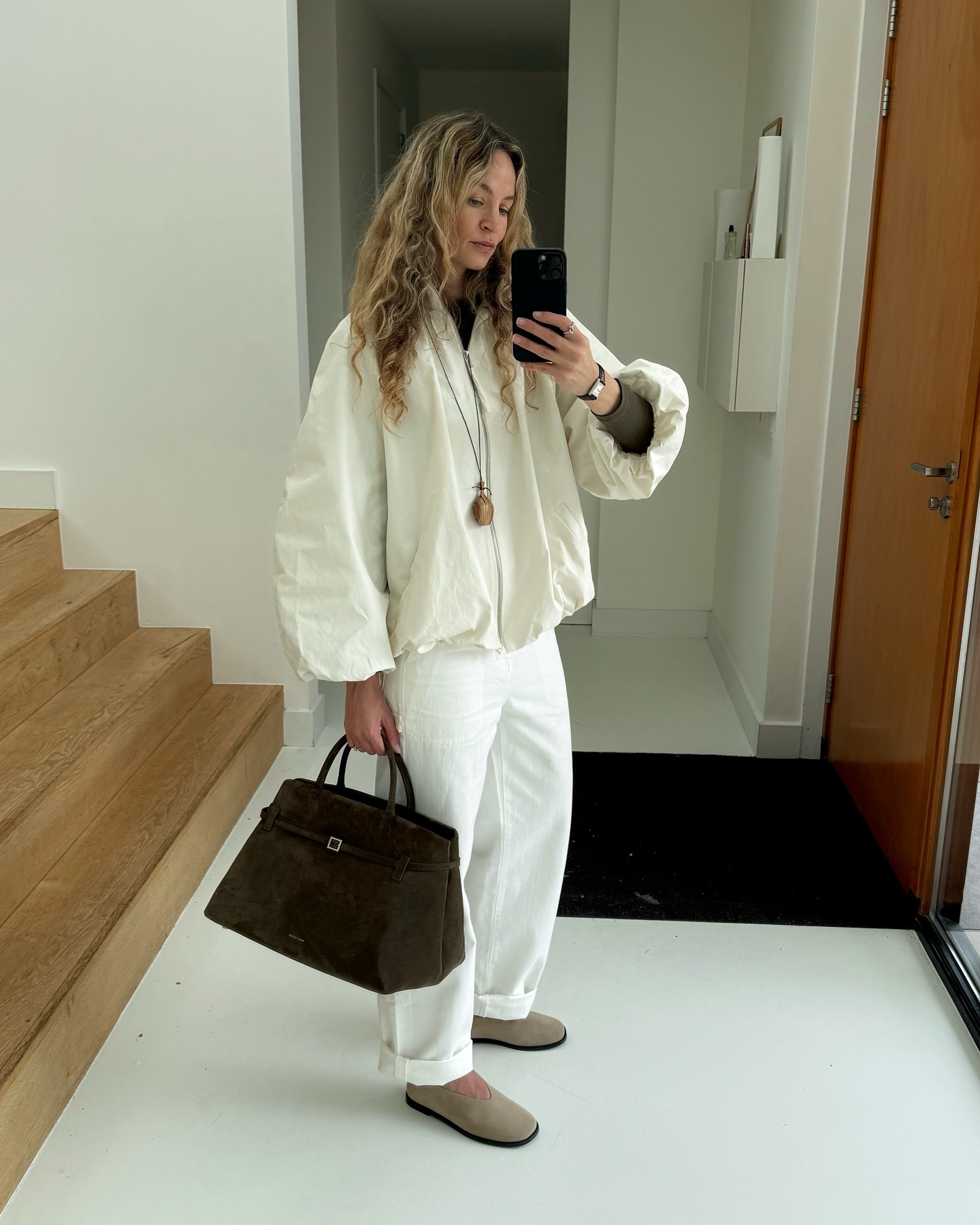 @anoukyve wearing a cream sporty jacket with cuffed white jeans and tan flats.