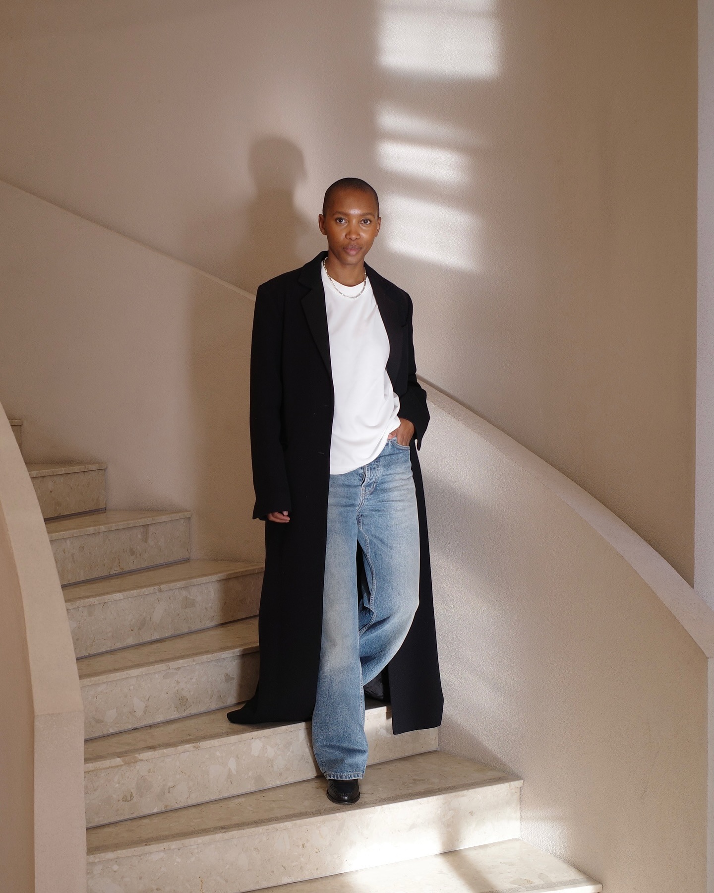 Marisa Martins wearing a long black coat, white tee, and blue jeans.