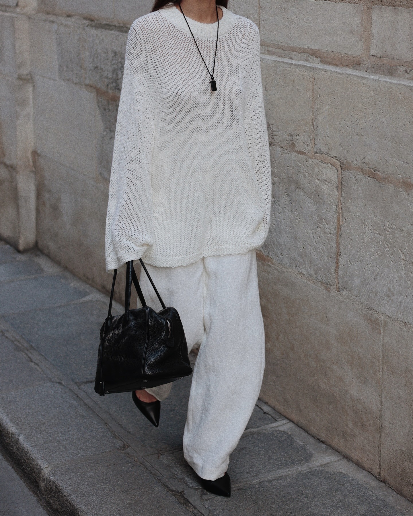 @modedamour wearing a white cotton oversize sweater, white barrel jeans, and black flats with a black bag.