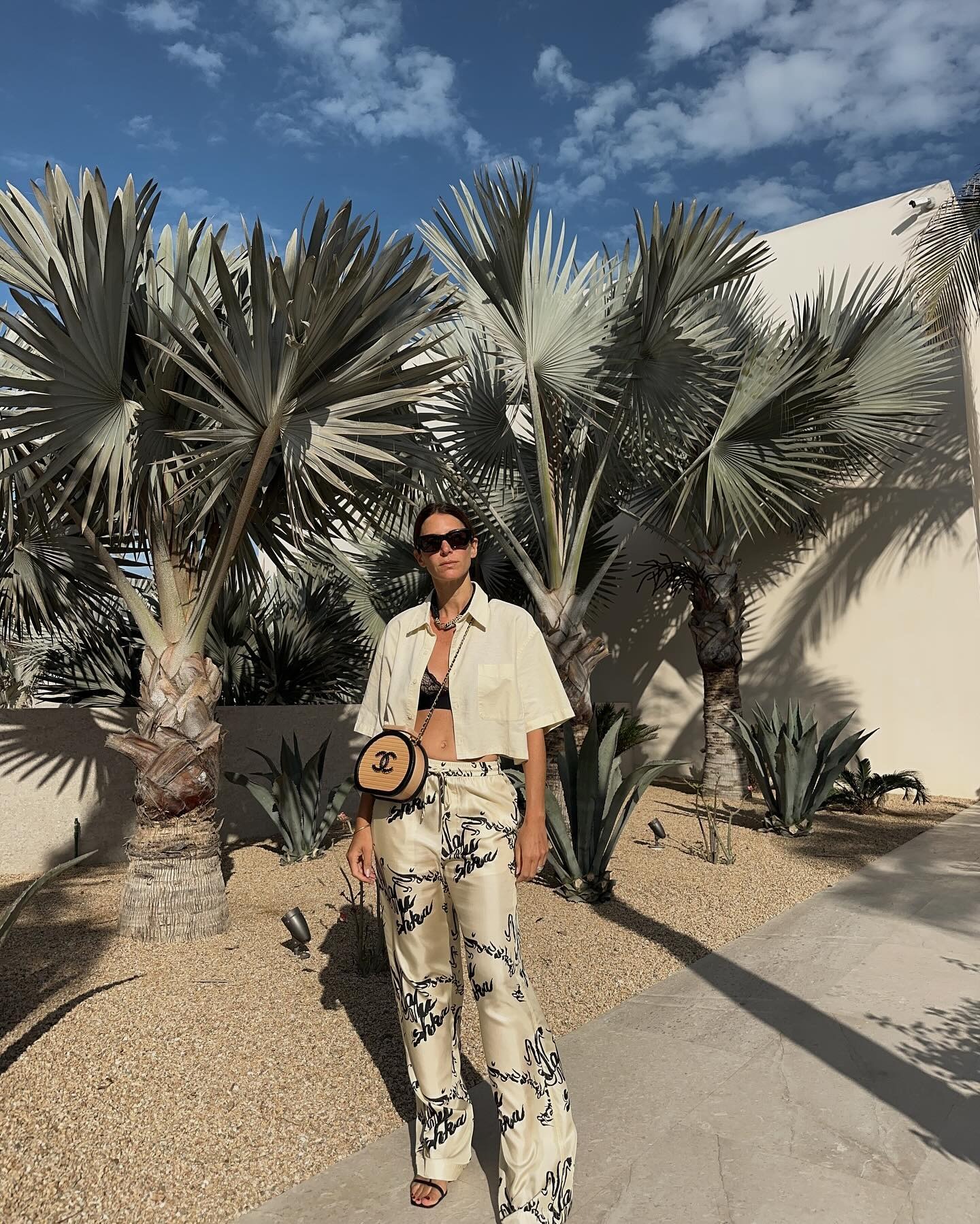 Jen wears a short-sleeve shirt, black bralette, printed silk pants, and a Chanel raffia bag.