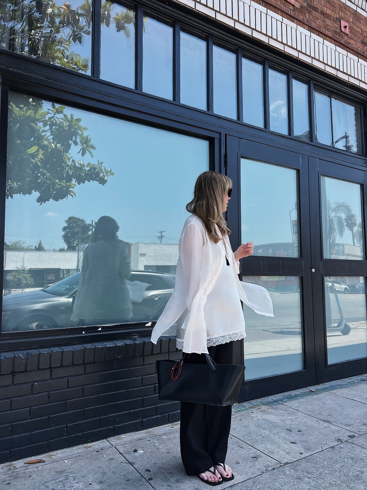 Jen Andrews Cater wearing an open white button-down over a lace-trimmed white tank and black trousers.