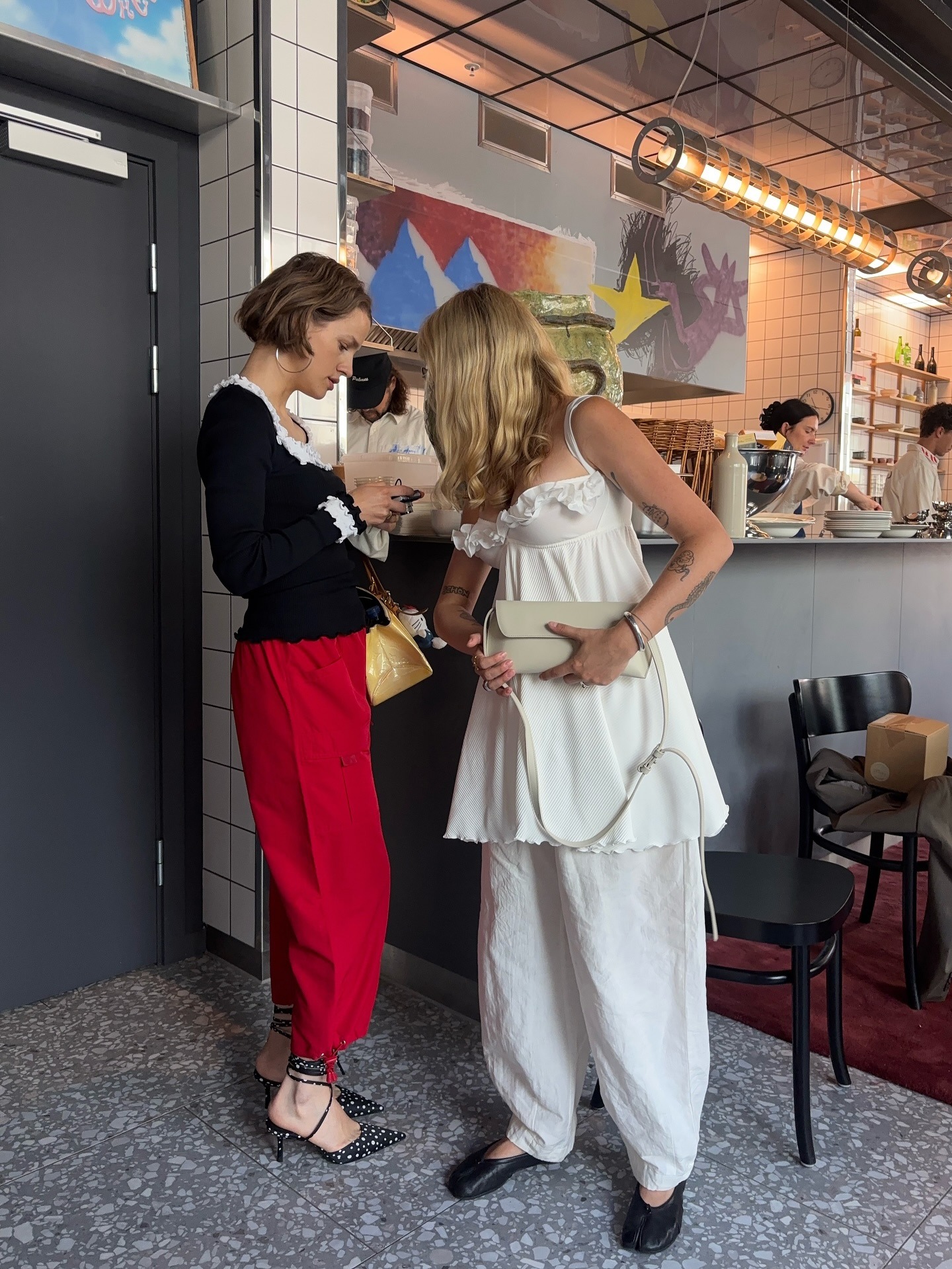A woman wearing red pants and a black longsleeve shirt and a woman wearing an all white outfit and black flats