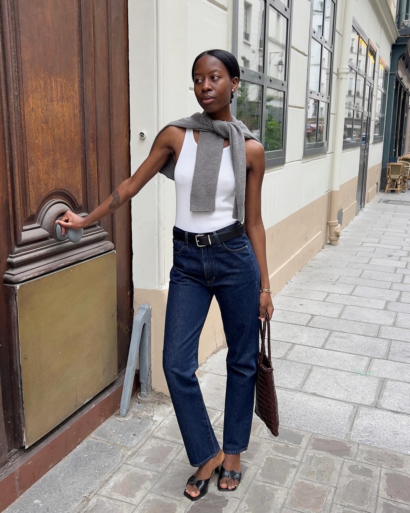 Influencer Sylvie wears dark wash denim with black kitten heels and a white tank. She also wears a grey sweater.
