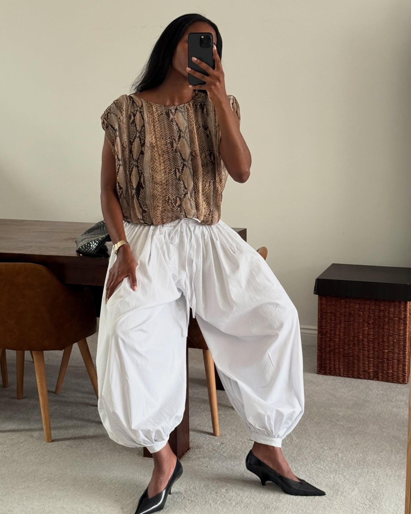 A woman wearing large white pants, a croc print top, and black pointed toe heels