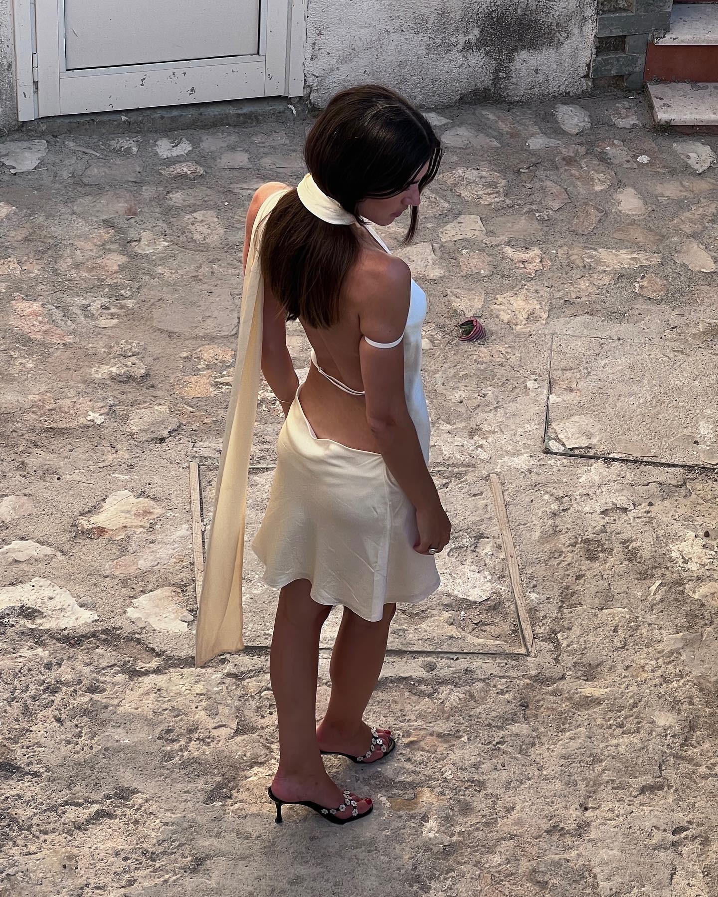 A woman wears an open back silk dress and mules.