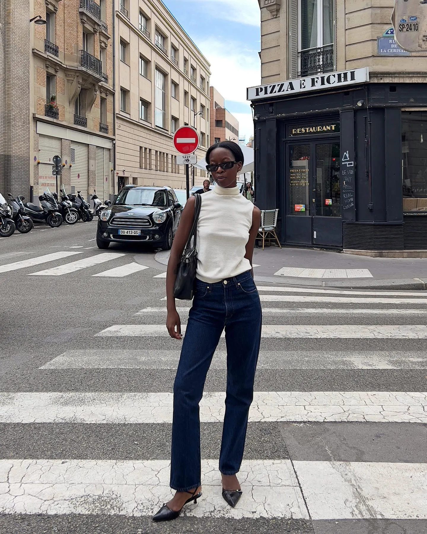 @sylviemus_ wearing white sweater, dark wash jeans, and black accessories posing on the street