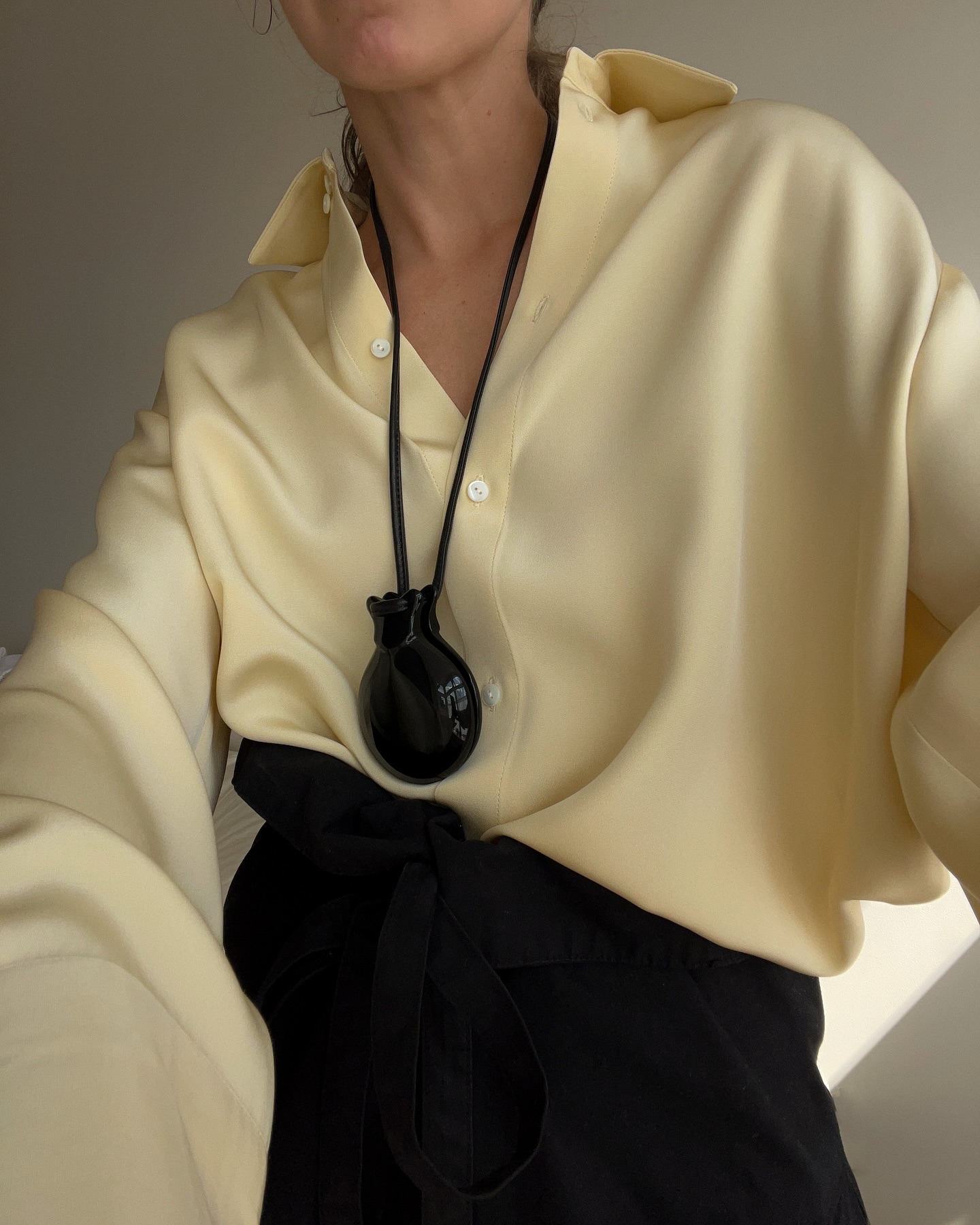 A woman wearing a yellow longsleeve top and black-cord pendant necklace