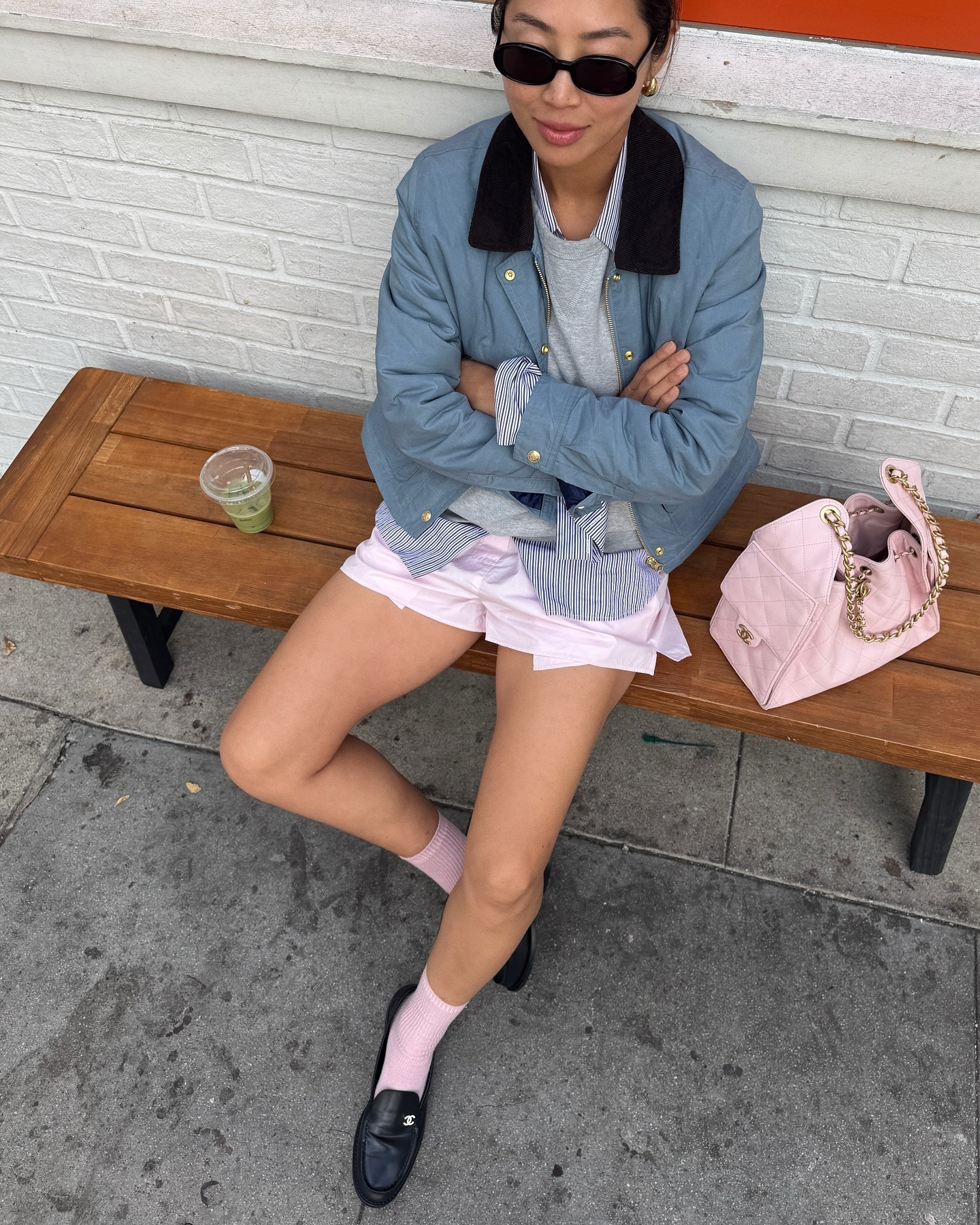 Aimee wears a blue jacket, pink shorts, pink socks, black loafers, and pink chanel bag.