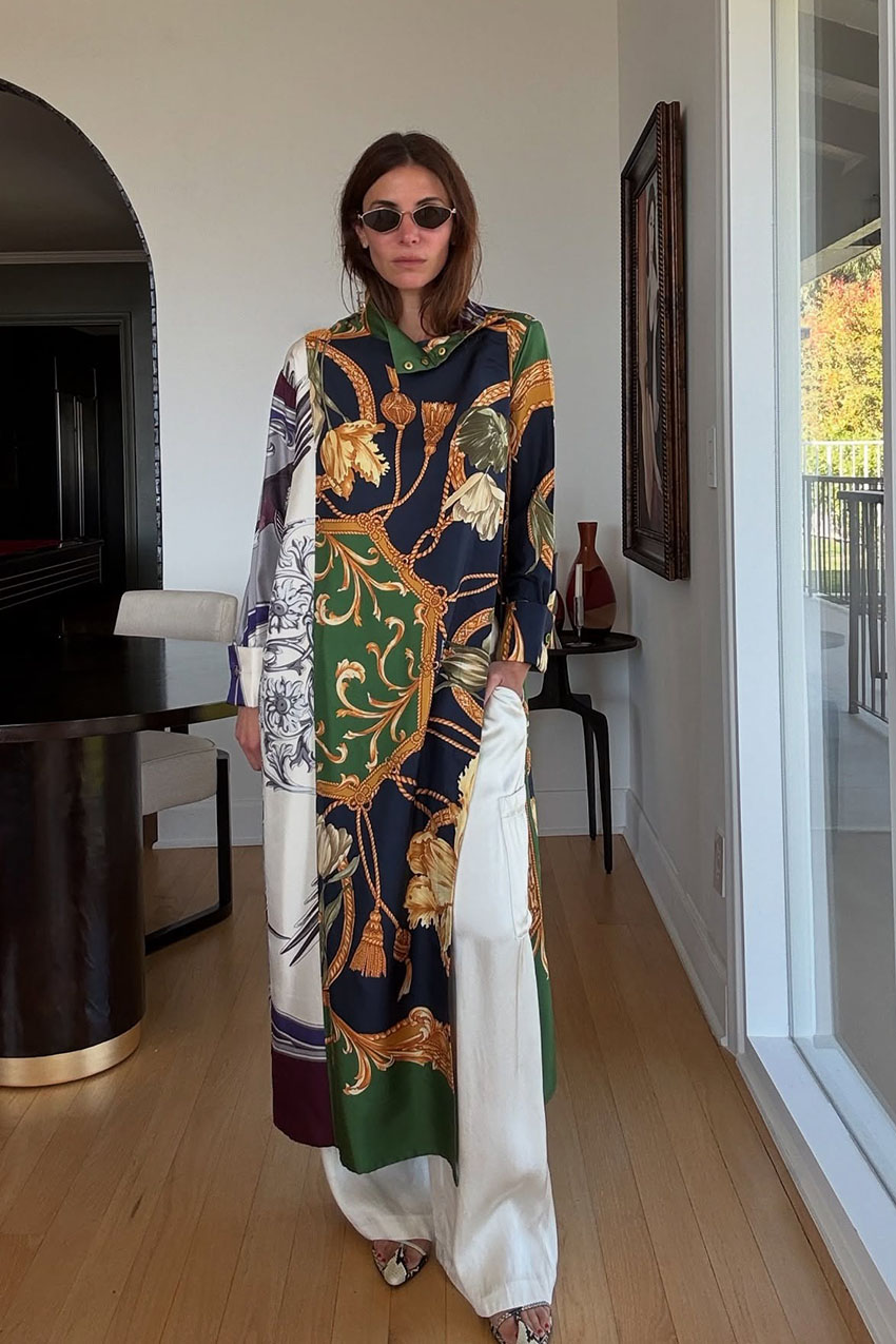 A woman wearing a multicolor dress over white pants with snakeskin boots