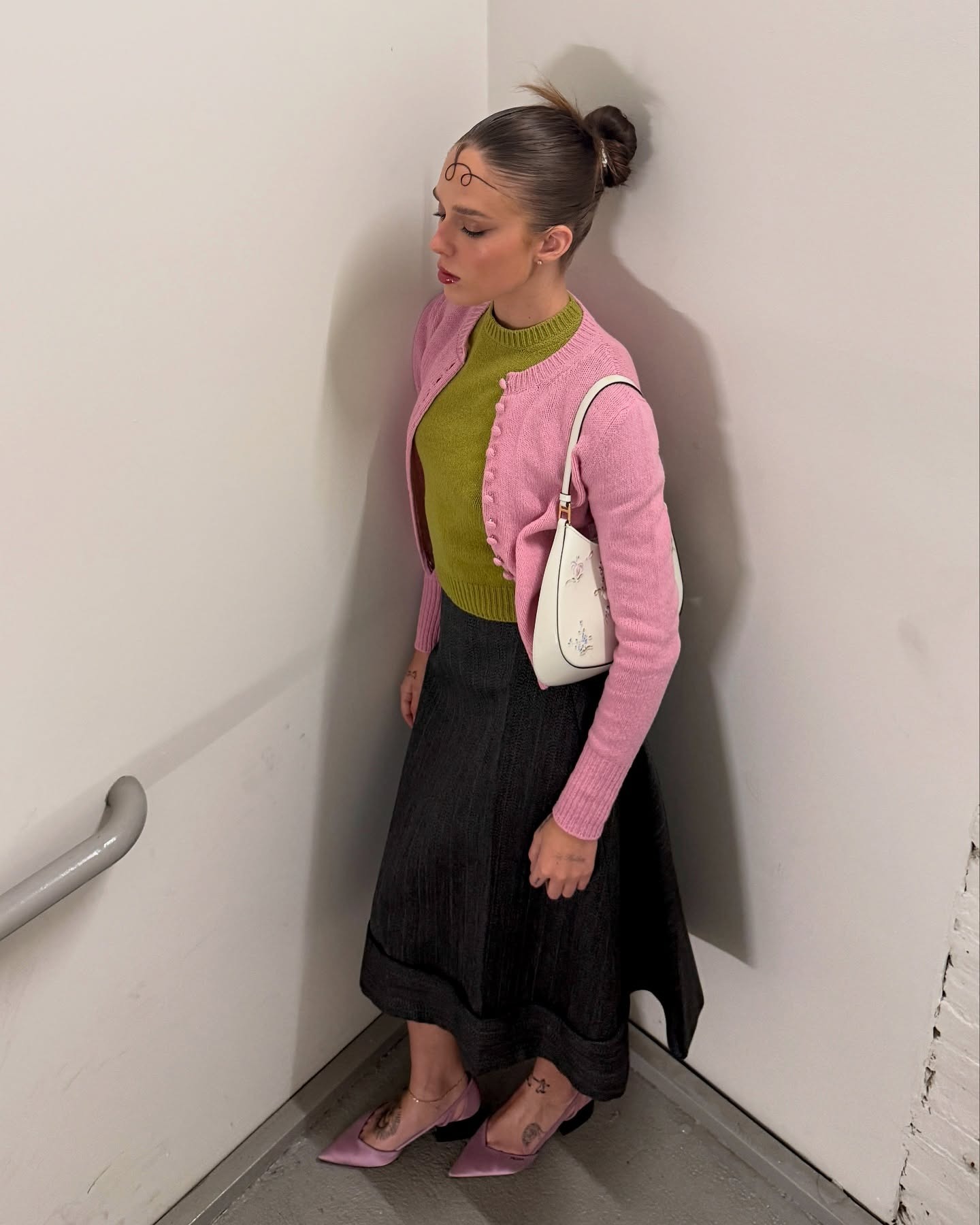 Lucy wears a pink cardigan, green sweater, denim skirt and pink satin heels.