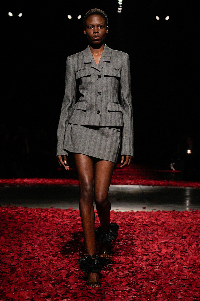 A Ferragamo model wearing a gray blazer and matching gray mini skirt, and black sandals