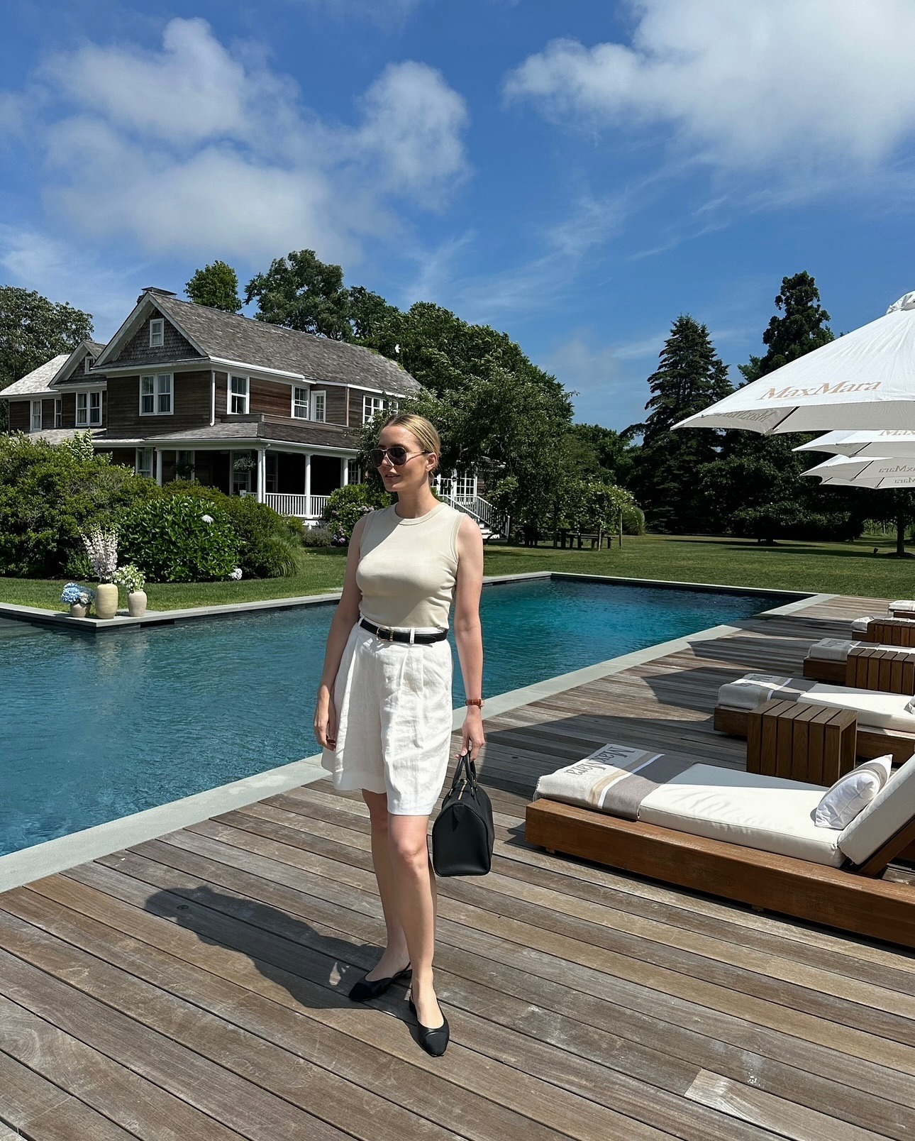 Kristen wears a beige tank, black belt, white shorts, and black ballet flats.