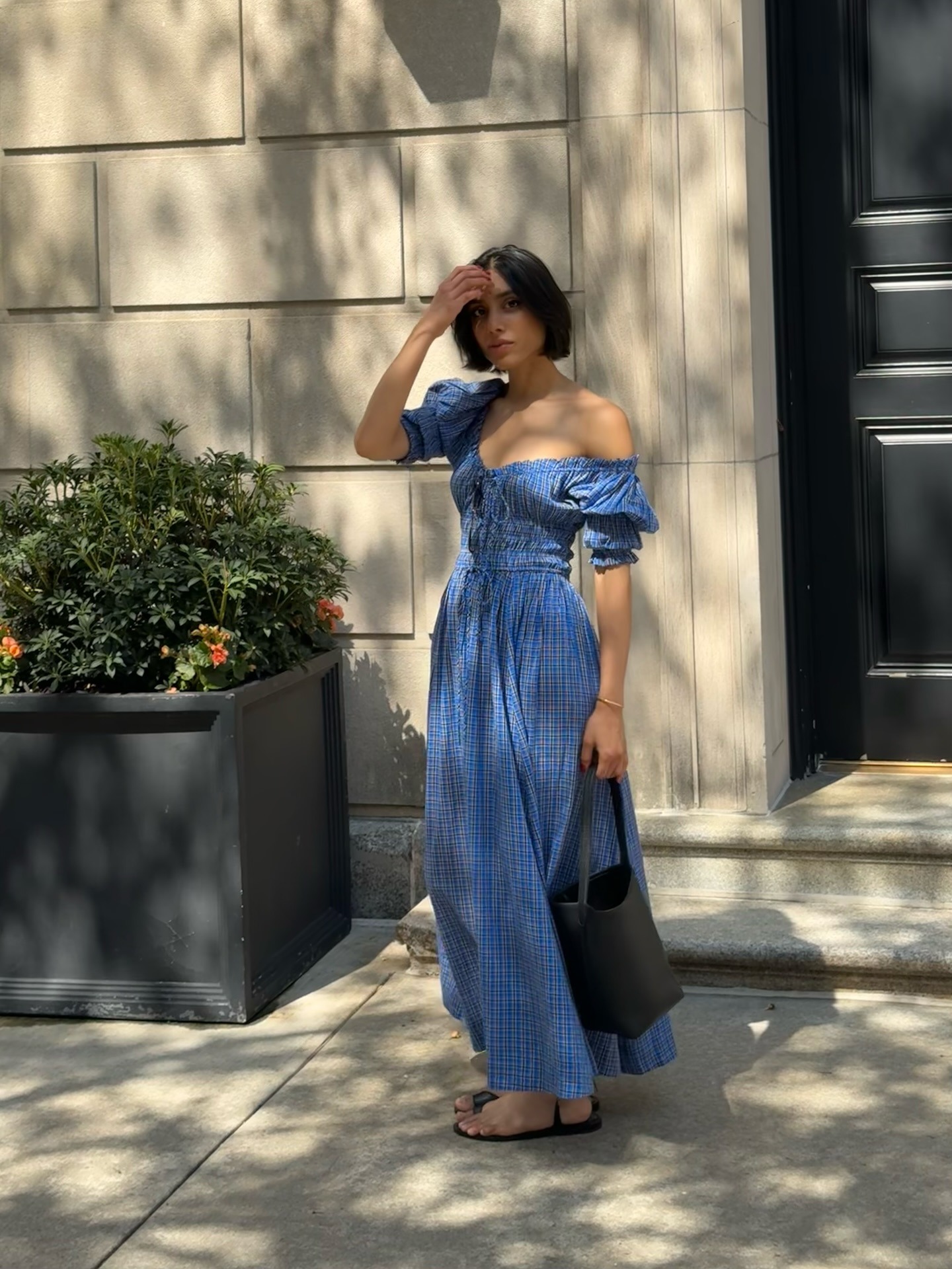 Shay wears a blue maxi dress, sandals, and black leather bag.