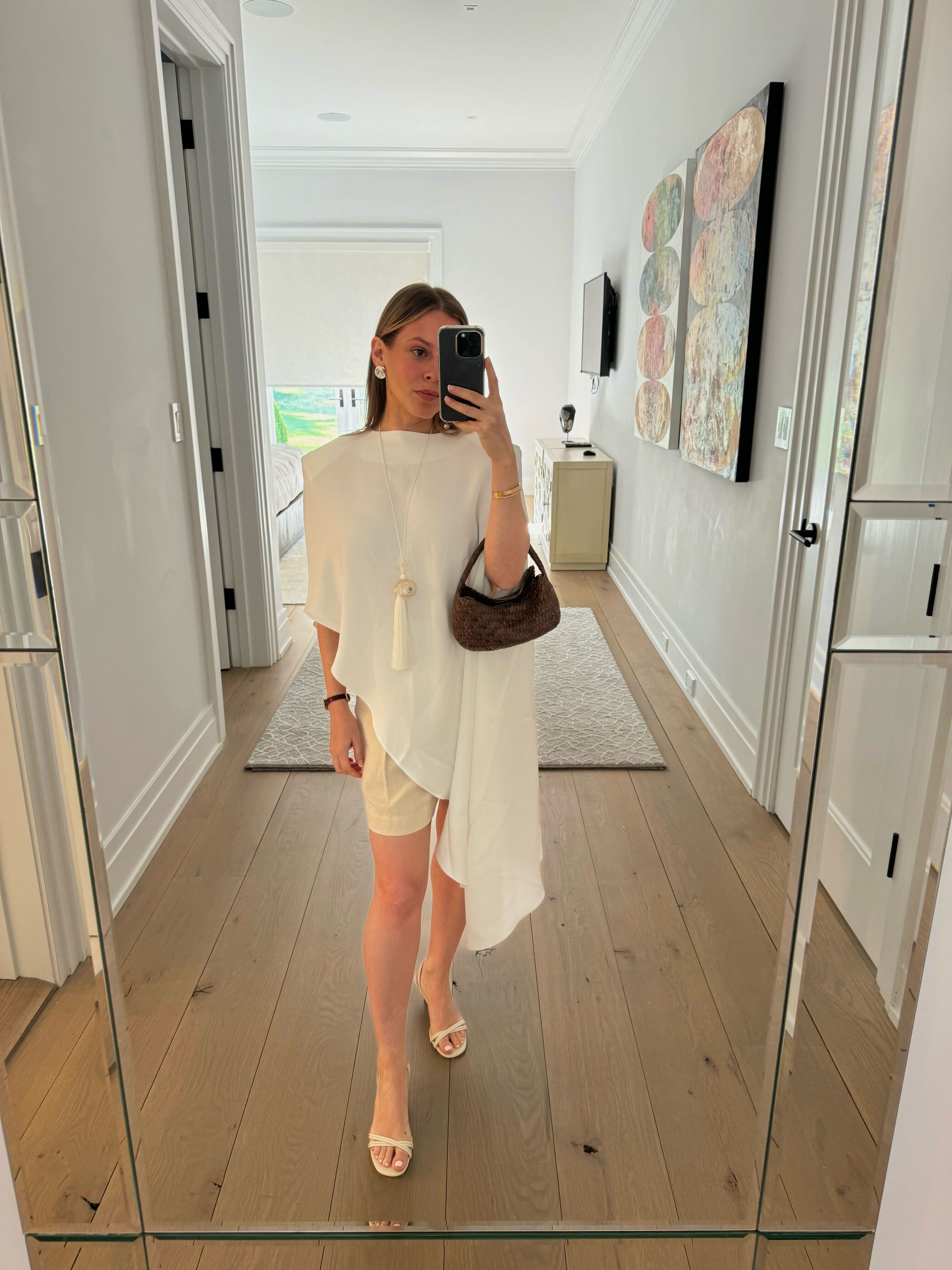 Nikki wears a white cape, linen shorts, and white flats.