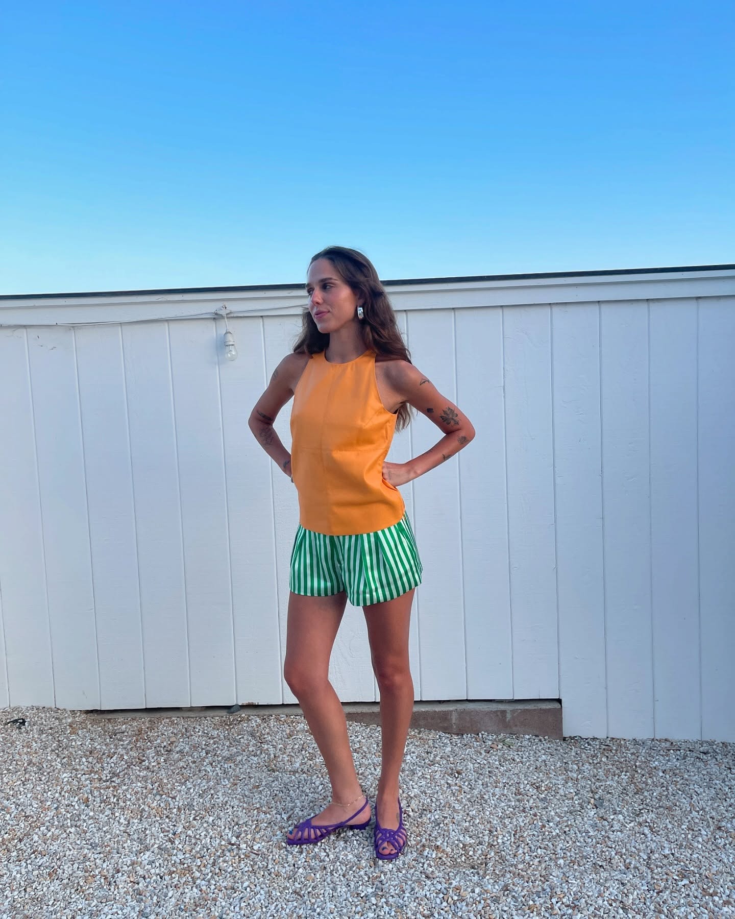lucy wears an orange top, green stripe shorts, and purple flats.