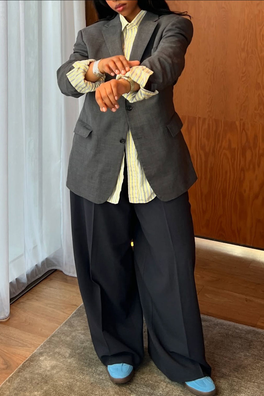 A woman wearing a gray blazer, black pants, yellow button-down, and blue suede sneakers