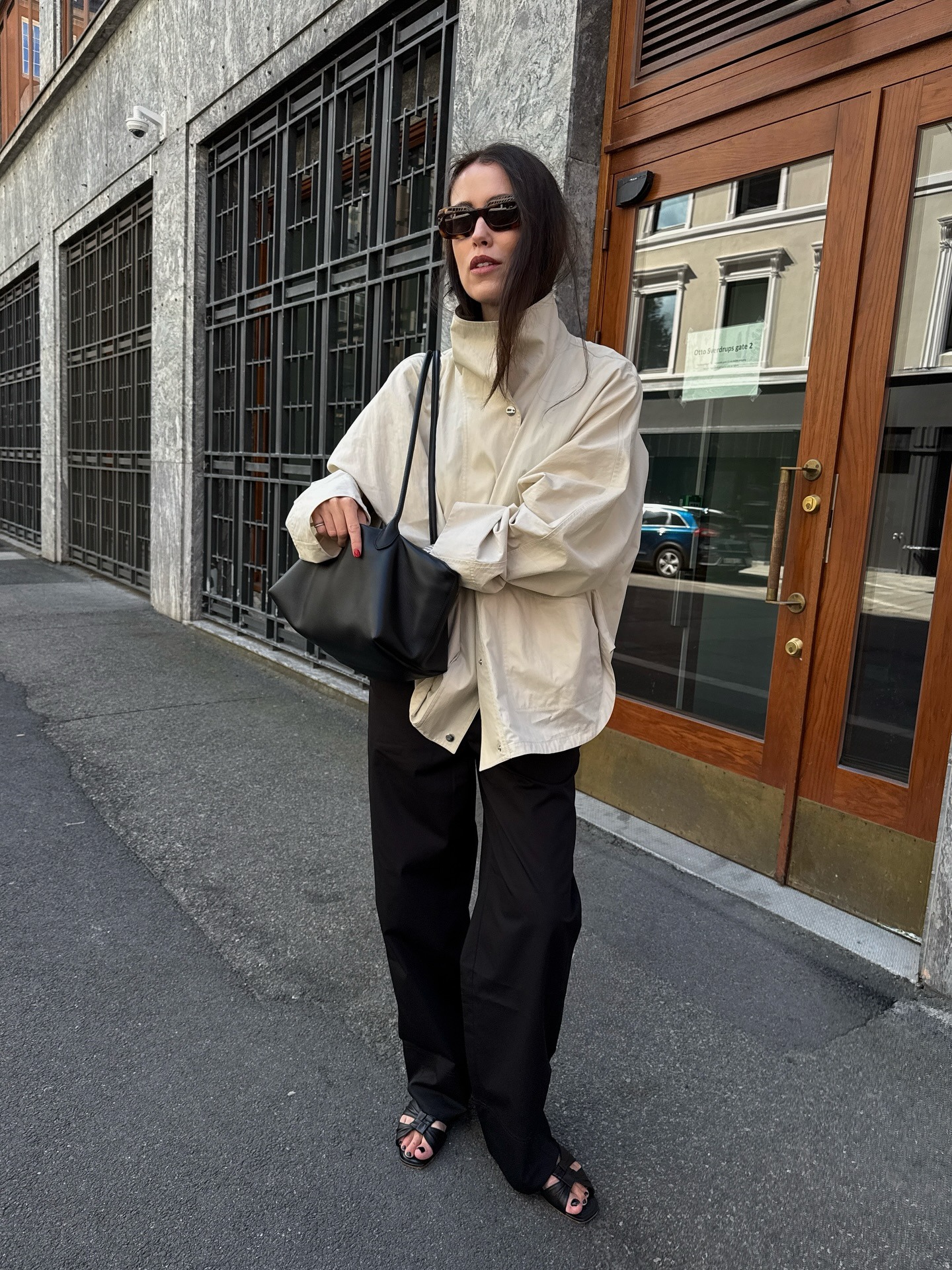 Annabel wears an ivory technical jacket, black pants, black sandals, and a black shoulder bag.